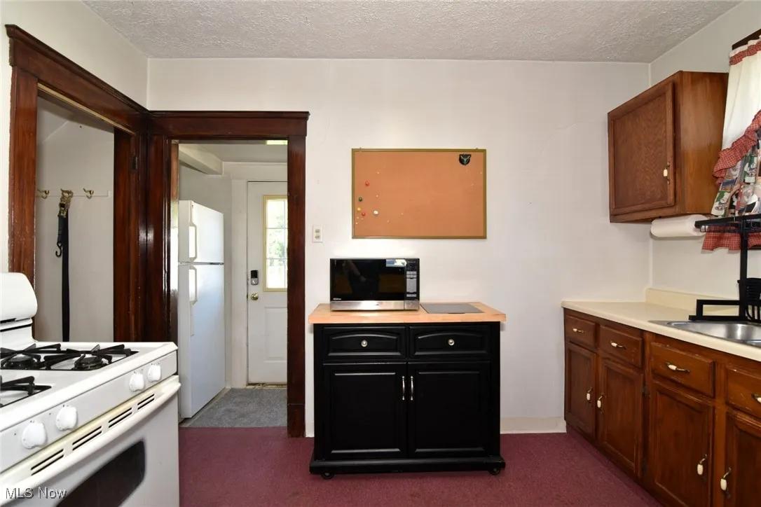 Kitchen featuring white appliances, light countertops, dark carpet, and a textured ceiling