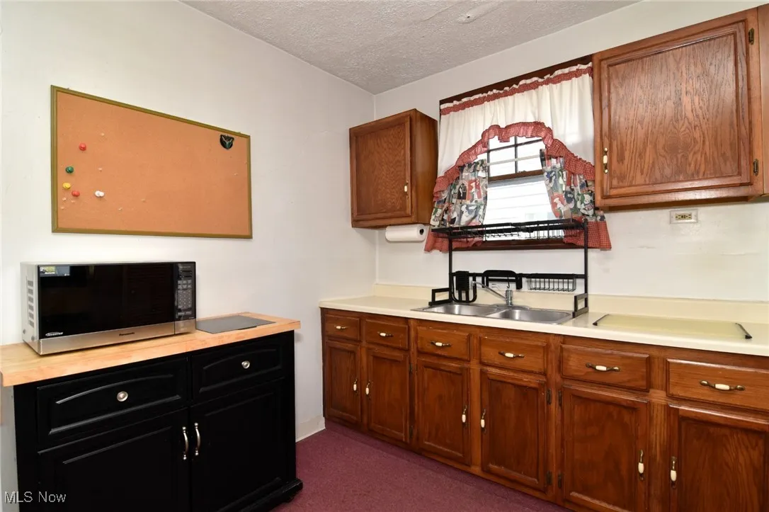 Kitchen with light countertops, stainless steel microwave, a textured ceiling, and dark carpet