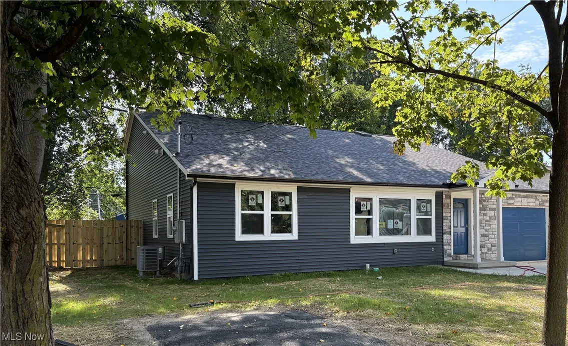 View of front of property with a garage, roof with shingles, and stone siding