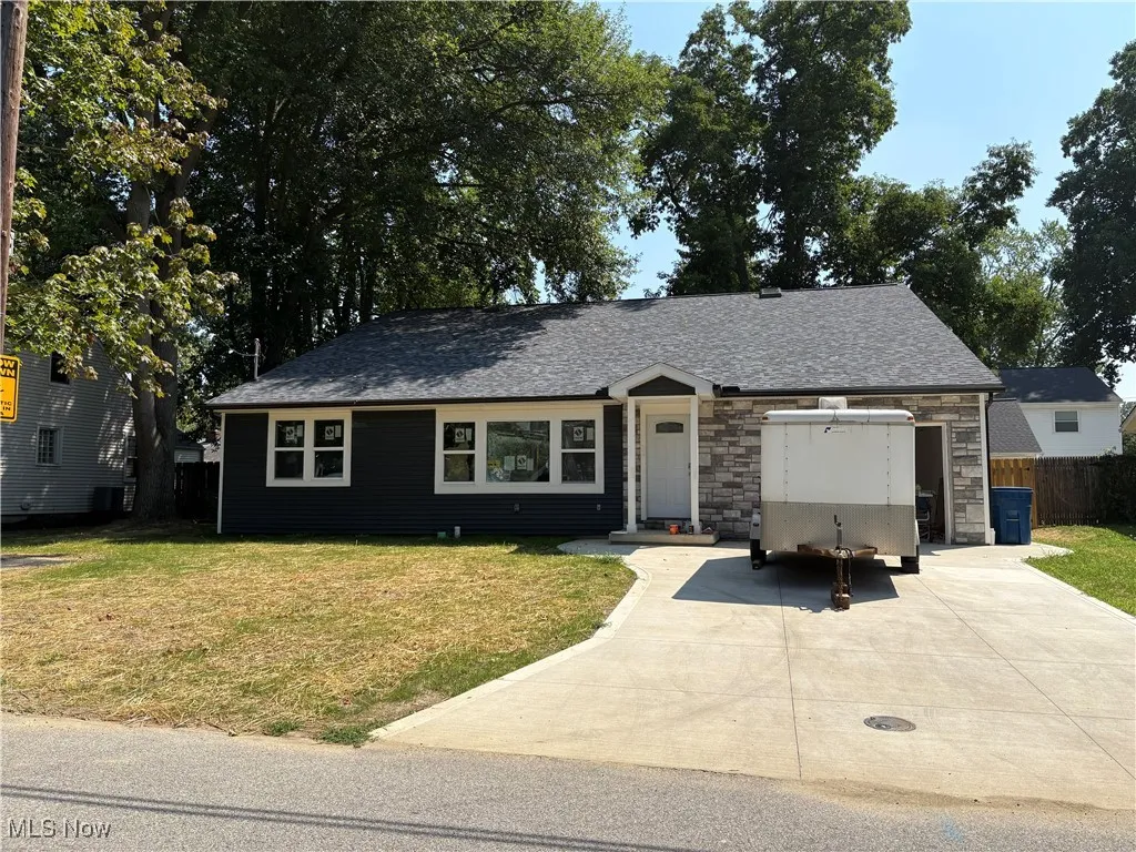 Two story home with concrete driveway, stone siding, and a shingled roof