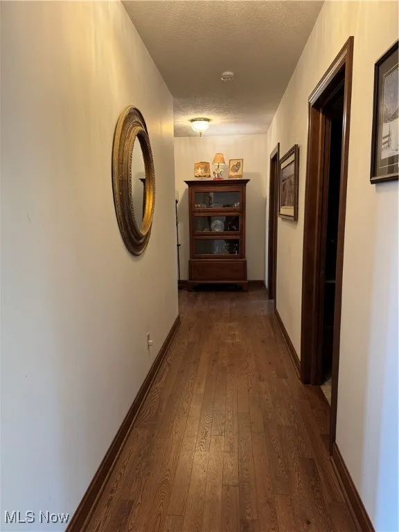 Hallway featuring a textured ceiling and dark wood finished floors