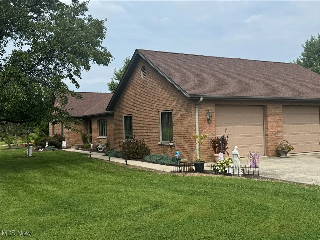 Back of house with a shingled roof, brick siding, a yard, and driveway