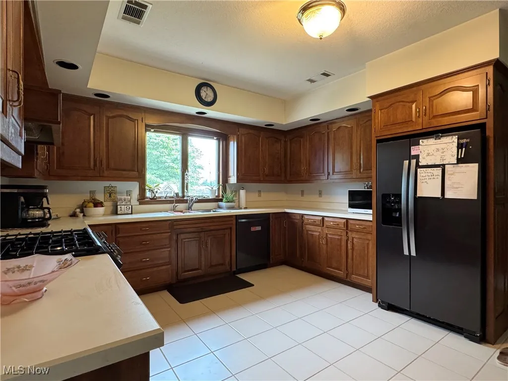 Kitchen with black appliances, light countertops, light tile patterned floors, and brown cabinetry