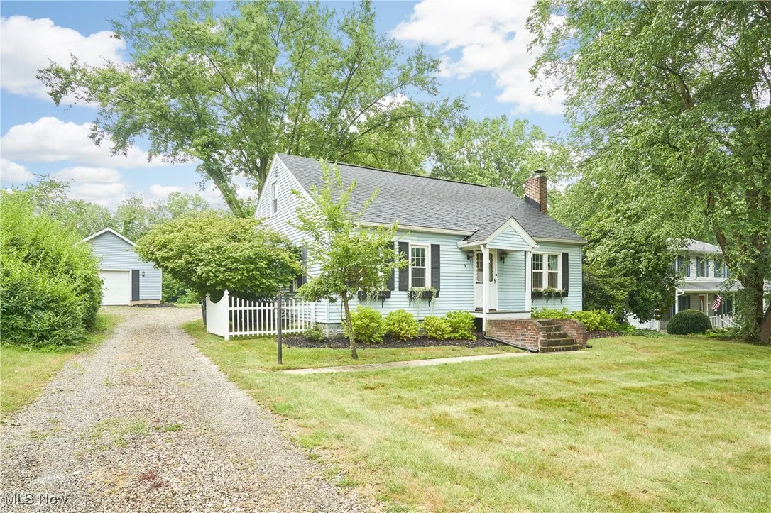 View of front of house with a chimney, an outdoor structure, a shingled roof, a garage, and gravel driveway