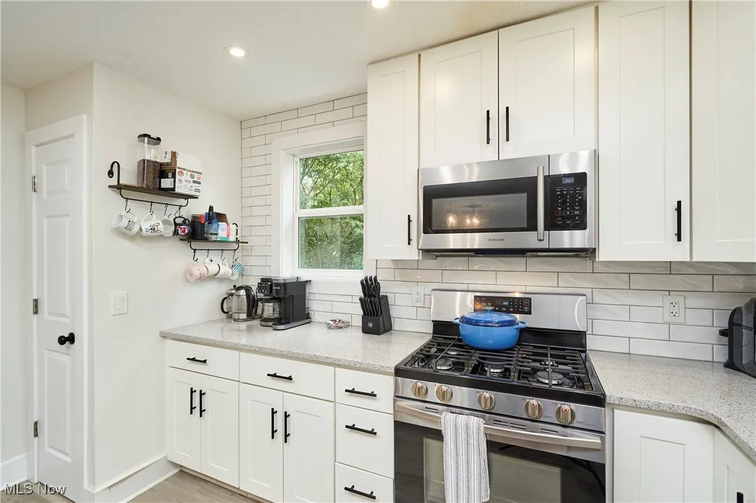 Kitchen with appliances with stainless steel finishes, white cabinetry, tasteful backsplash, light stone counters, and light wood-style flooring