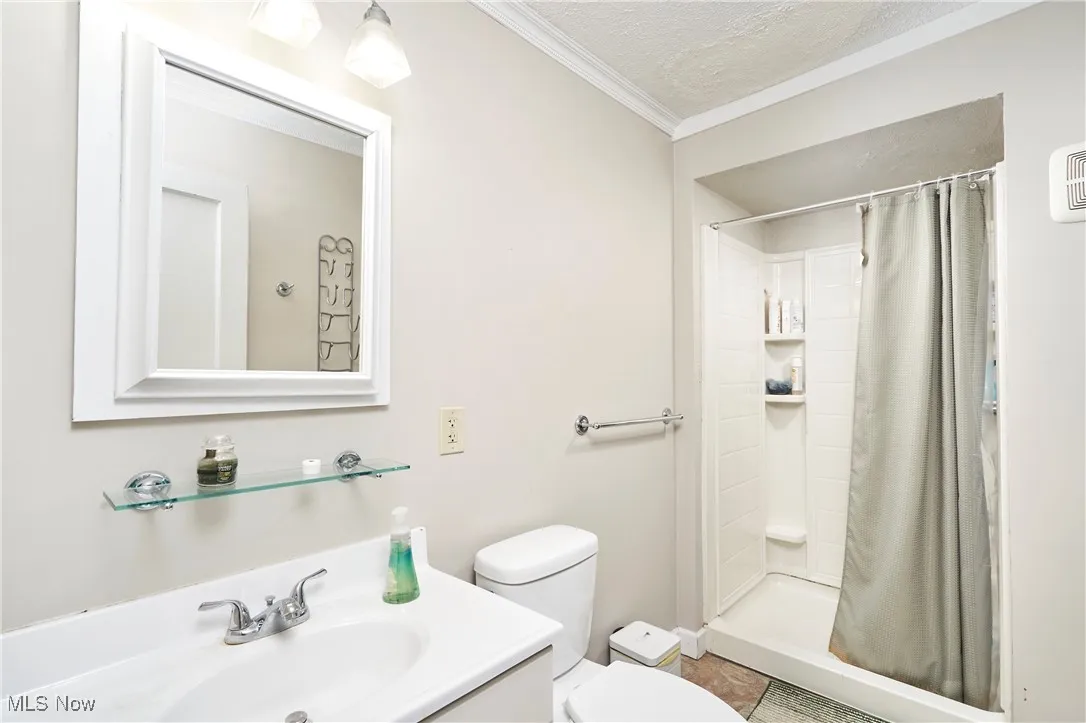 Bathroom featuring a textured ceiling, vanity, a shower stall, and ornamental molding