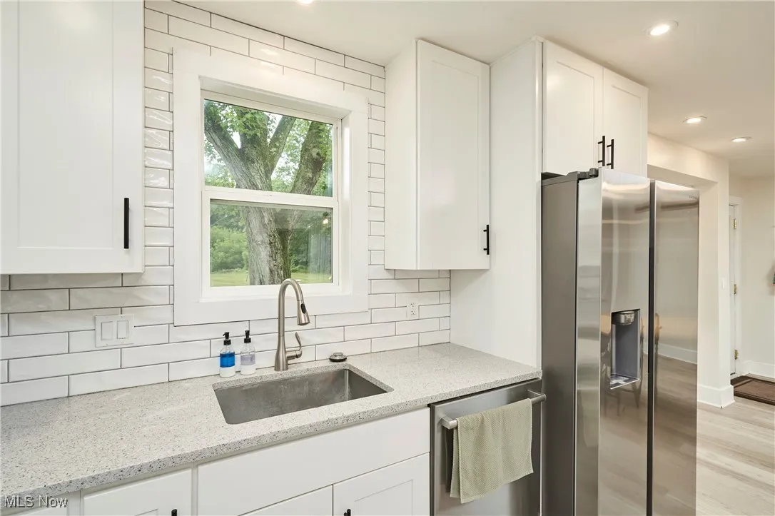 Kitchen with appliances with stainless steel finishes, light stone counters, white cabinets, recessed lighting, and light wood finished floors