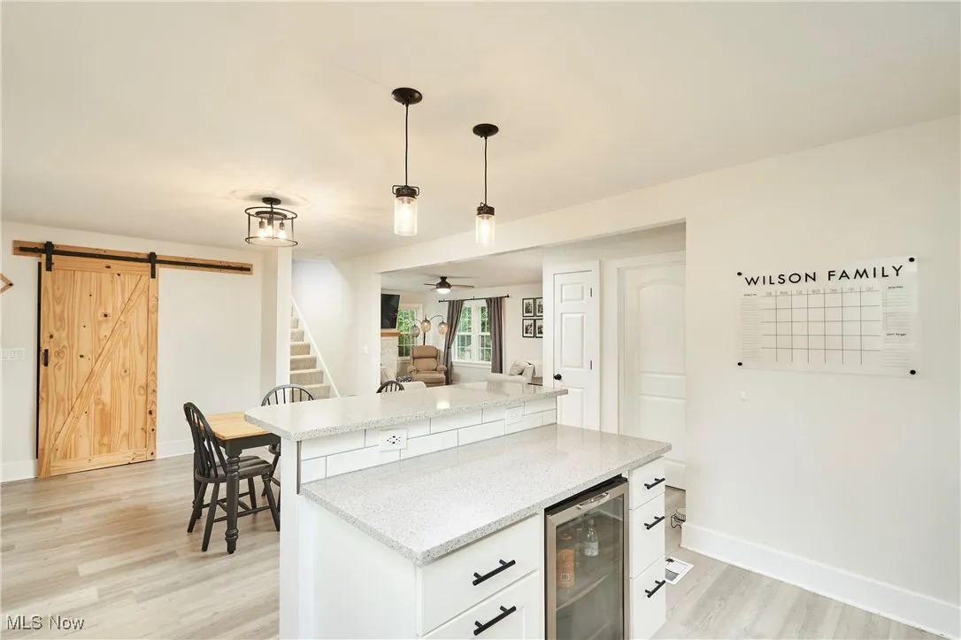 Kitchen featuring beverage cooler, decorative light fixtures, light wood finished floors, light stone countertops, and a barn door
