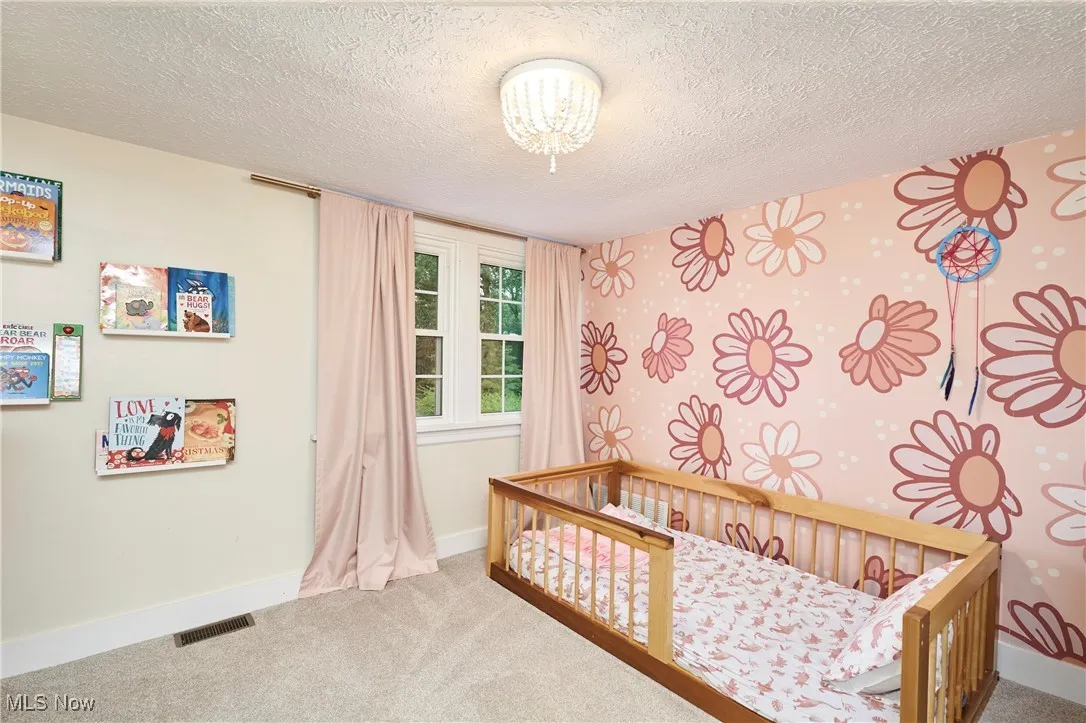 Carpeted bedroom with a nursery area, a textured ceiling, and a chandelier