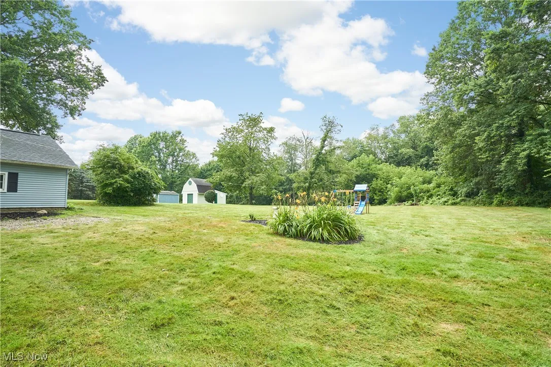 View of grassy yard with a playground and an outbuilding