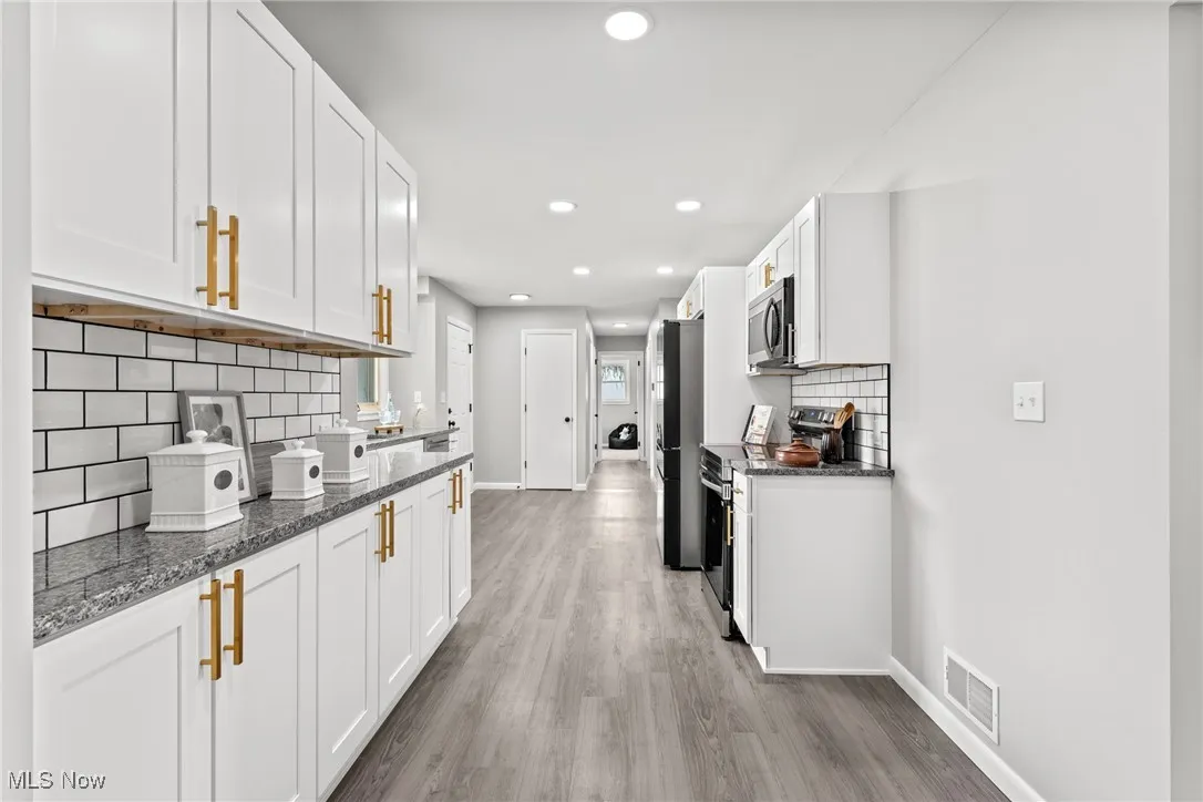Kitchen featuring decorative backsplash, dark stone counters, stainless steel appliances, white cabinetry, and recessed lighting