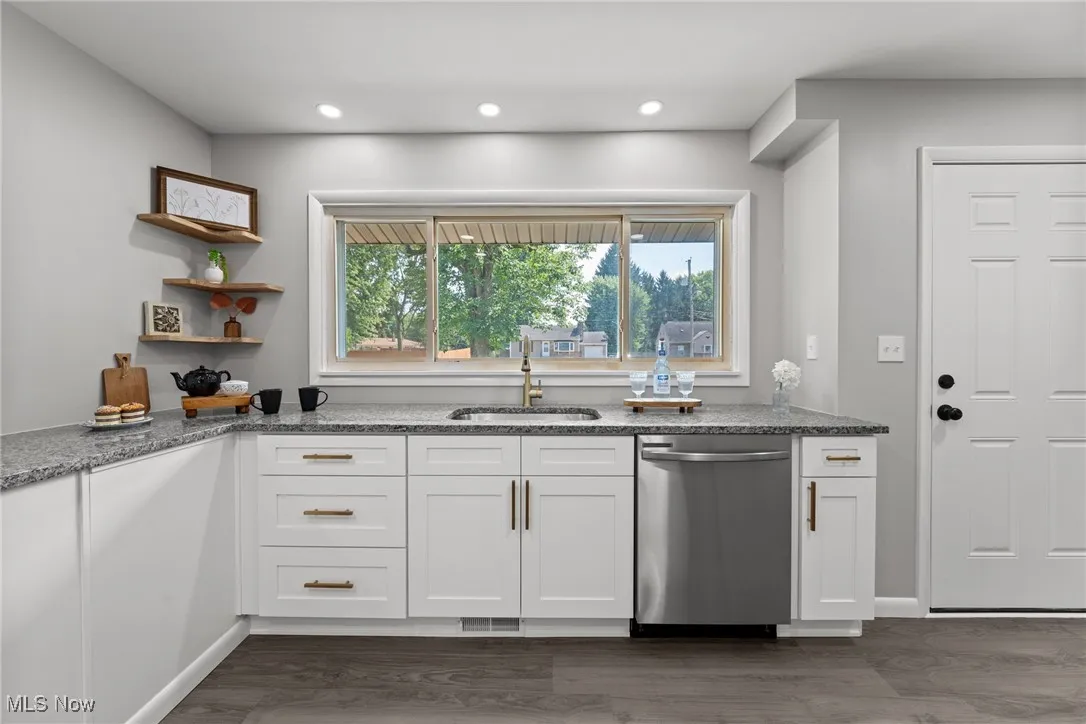 Kitchen with white cabinetry, open shelves, stainless steel dishwasher, dark stone counters, and dark wood-type flooring