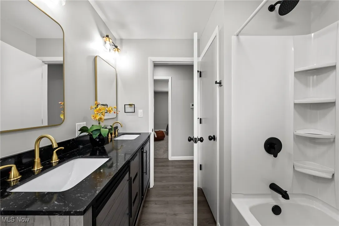 Full bath featuring washtub / shower combination, double vanity, and dark wood-style floors