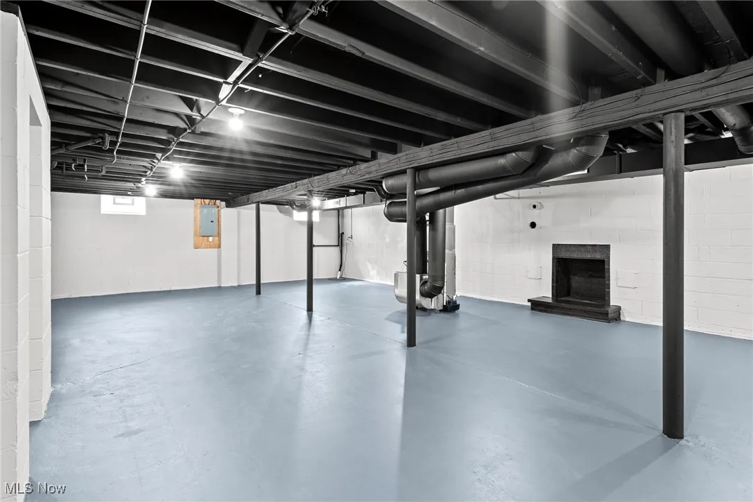 Below grade area featuring heating unit, electric panel, and a fireplace with raised hearth