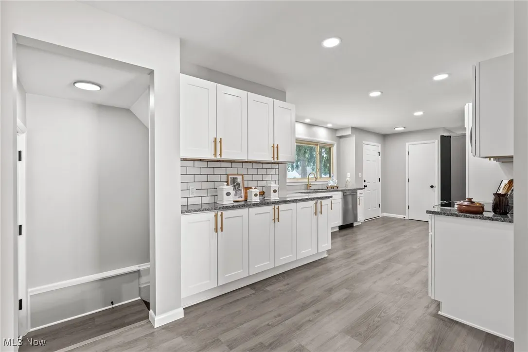 Kitchen featuring dark stone countertops, white cabinets, tasteful backsplash, light wood-style floors, and recessed lighting