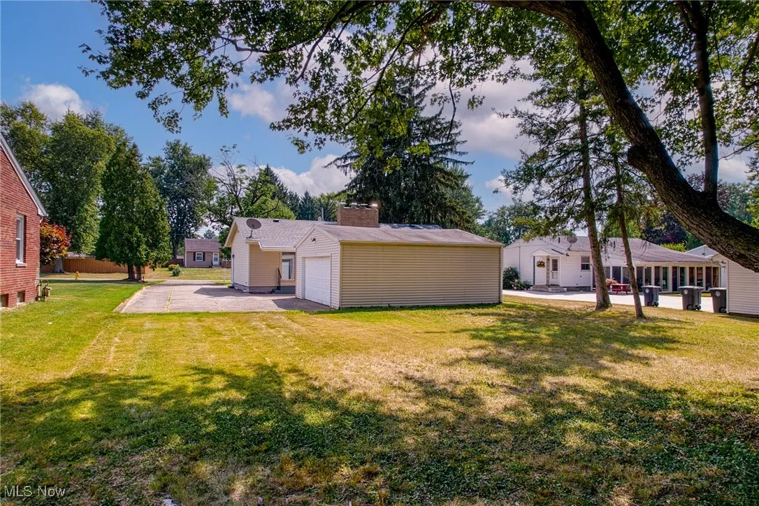 Back of property featuring a chimney, a patio, a garage, and a lawn