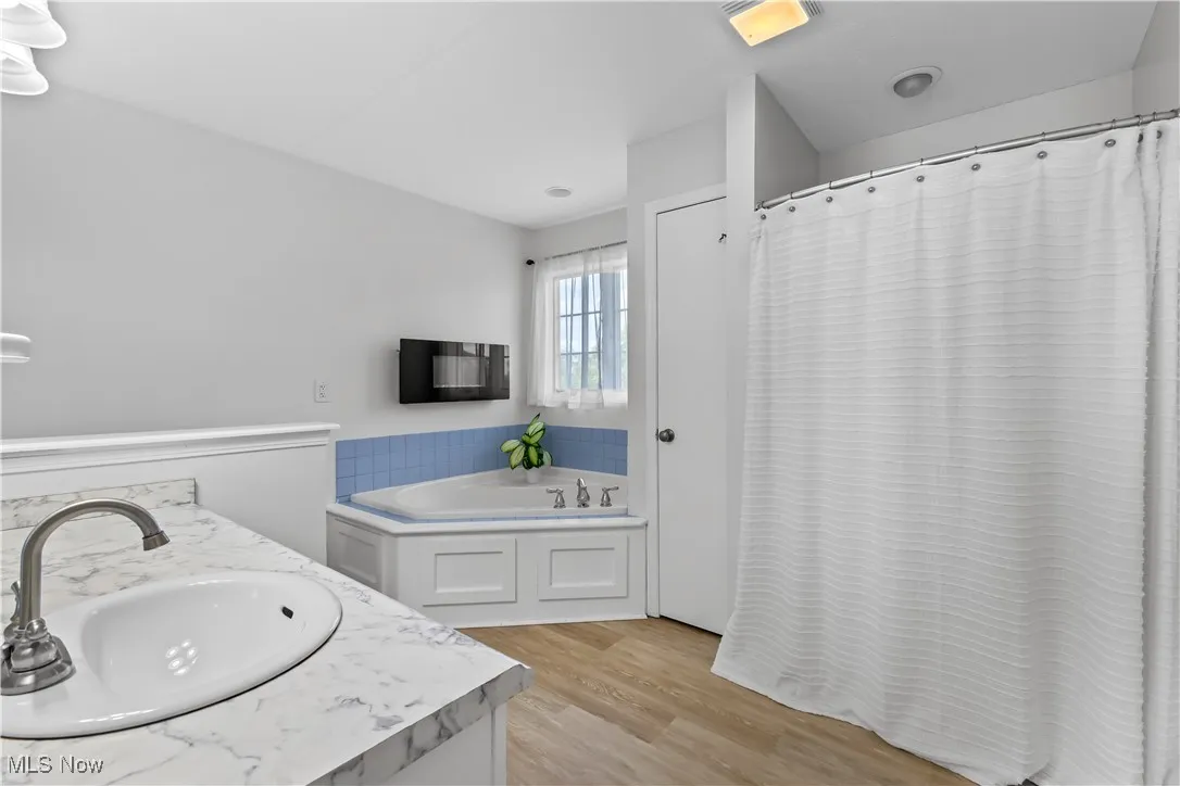 Bathroom with a bath, light wood finished floors, vanity, and a shower with shower curtain