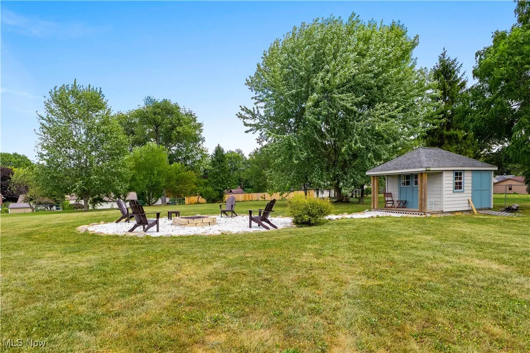 View of green lawn with a patio area, an outdoor fire pit, and an outbuilding