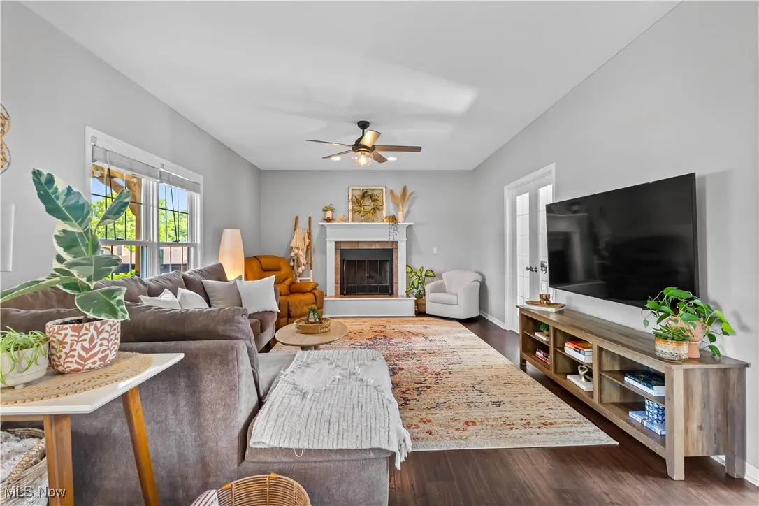 Living room featuring dark wood-type flooring, a ceiling fan, and a tile fireplace