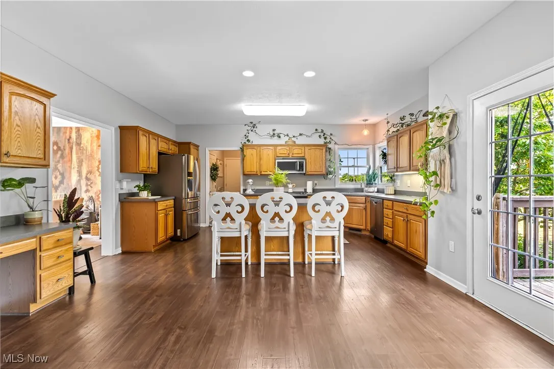 Kitchen featuring a breakfast bar area, dark wood finished floors, stainless steel appliances, a kitchen island, and brown cabinets