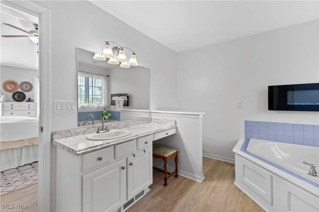 Ensuite bathroom featuring a garden tub, light wood-style floors, vanity, and a ceiling fan