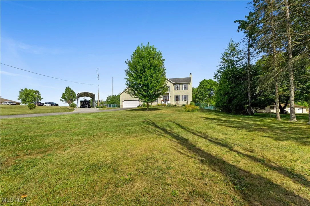 View of grassy yard with a carport, a garage, and asphalt driveway