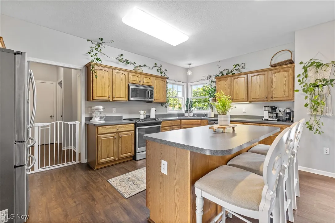 Kitchen with stainless steel appliances, dark countertops, a kitchen breakfast bar, a center island, and brown cabinets