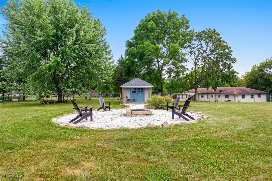 View of grassy yard featuring a fire pit, a patio area, and an outdoor structure