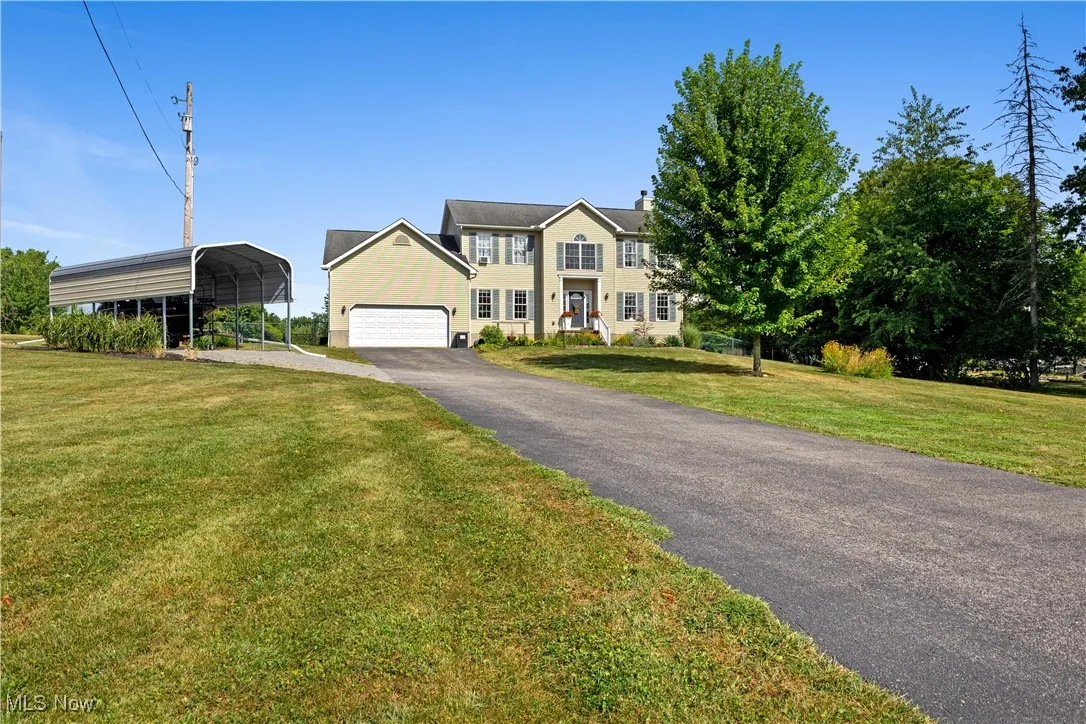 Colonial inspired home with a carport, asphalt driveway, a front lawn, a chimney, and a garage