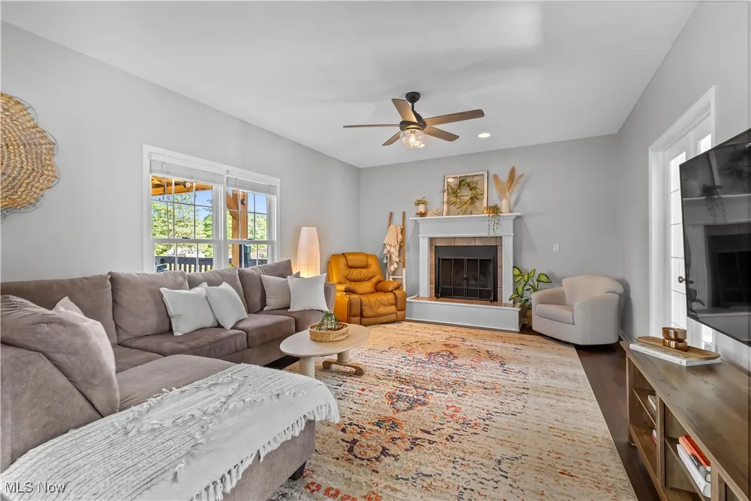 Living area with a tiled fireplace, ceiling fan, and wood finished floors