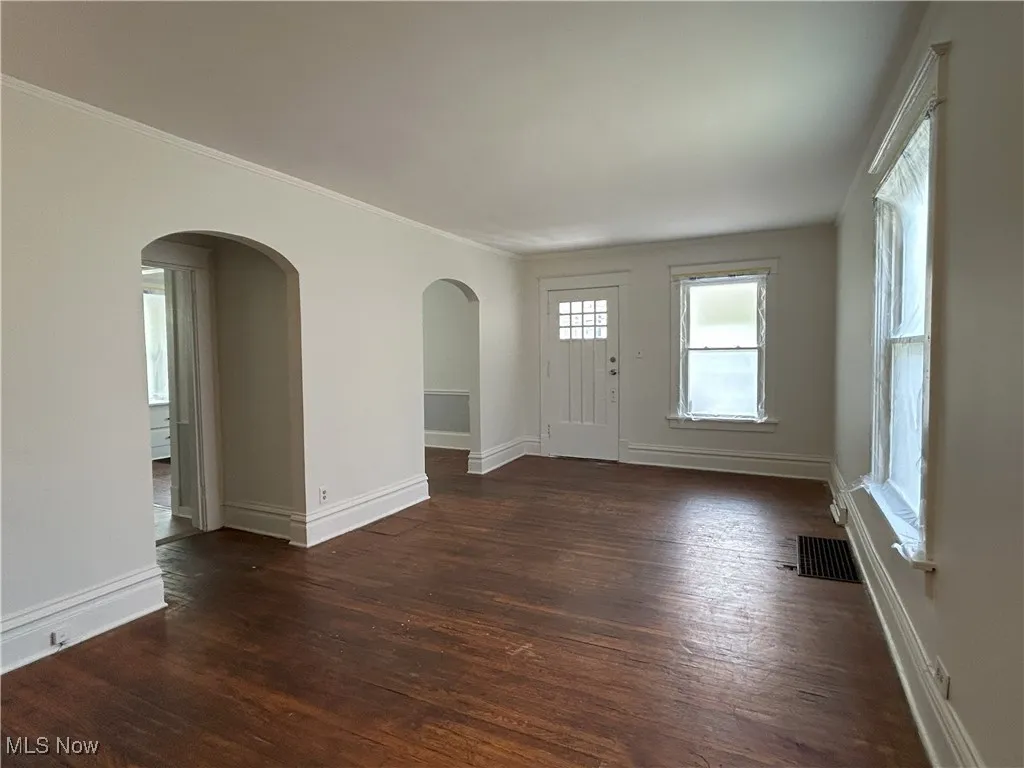 Foyer with dark wood-style floors, ornamental molding, and arched walkways