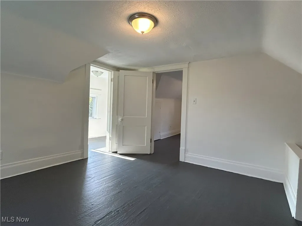 Bonus room with a textured ceiling, dark wood-type flooring, and lofted ceiling