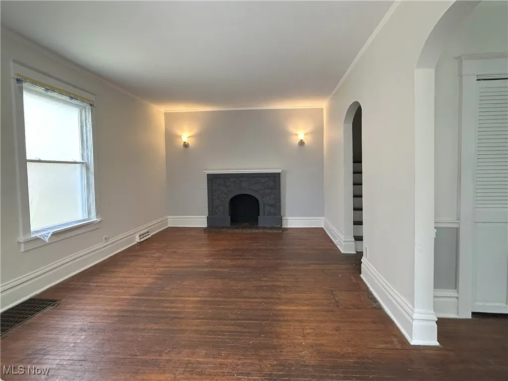Unfurnished living room with a high end fireplace, arched walkways, dark wood-style flooring, and ornamental molding