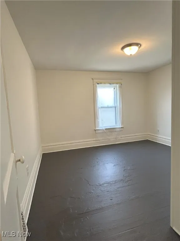 Unfurnished room featuring baseboards and dark wood finished floors
