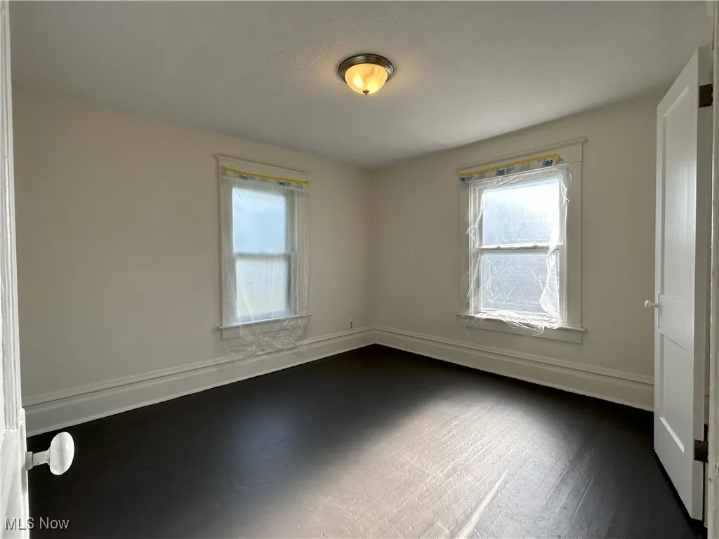 Empty room with baseboards and dark wood-type flooring