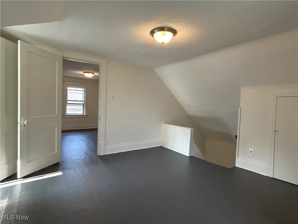Additional living space with dark wood-type flooring, vaulted ceiling, and a textured ceiling