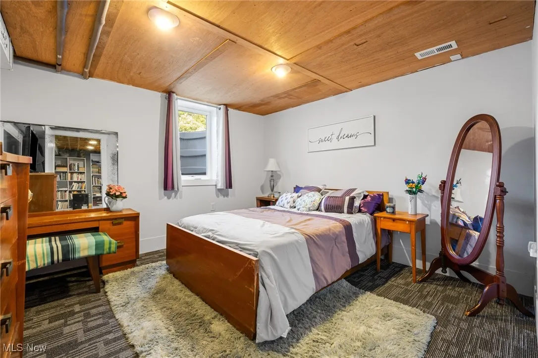 Bedroom with wooden ceiling and dark colored carpet
