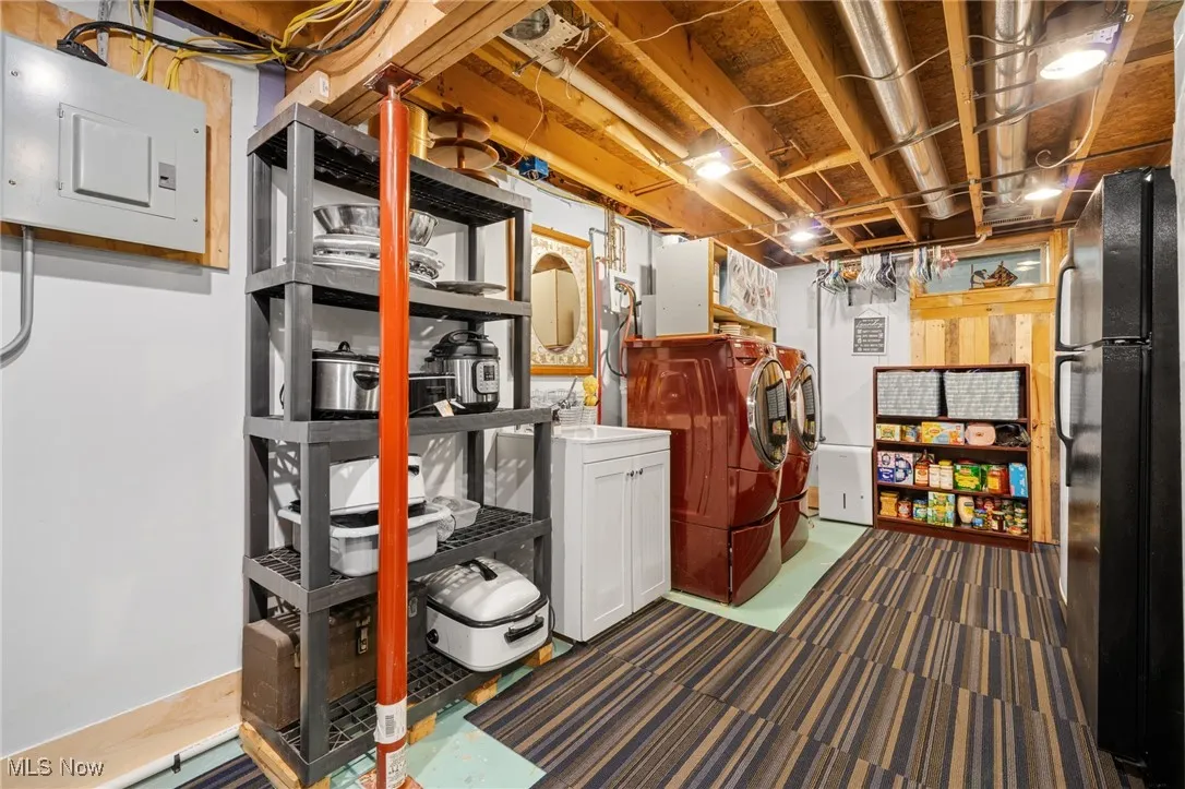 Unfinished basement featuring freestanding refrigerator, electric panel, and separate washer and dryer