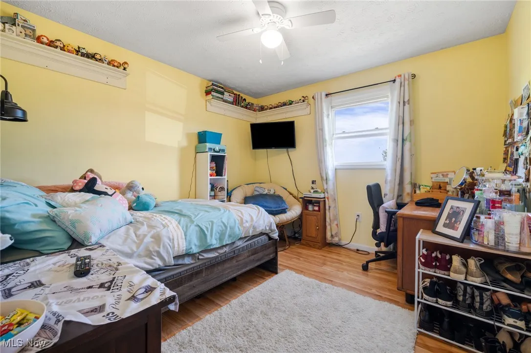 Bedroom featuring light wood-type flooring, ceiling fan, an office area, and a textured ceiling