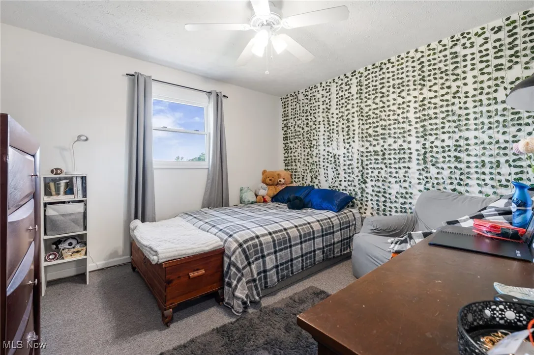 Bedroom featuring ceiling fan, dark colored carpet, and a textured ceiling
