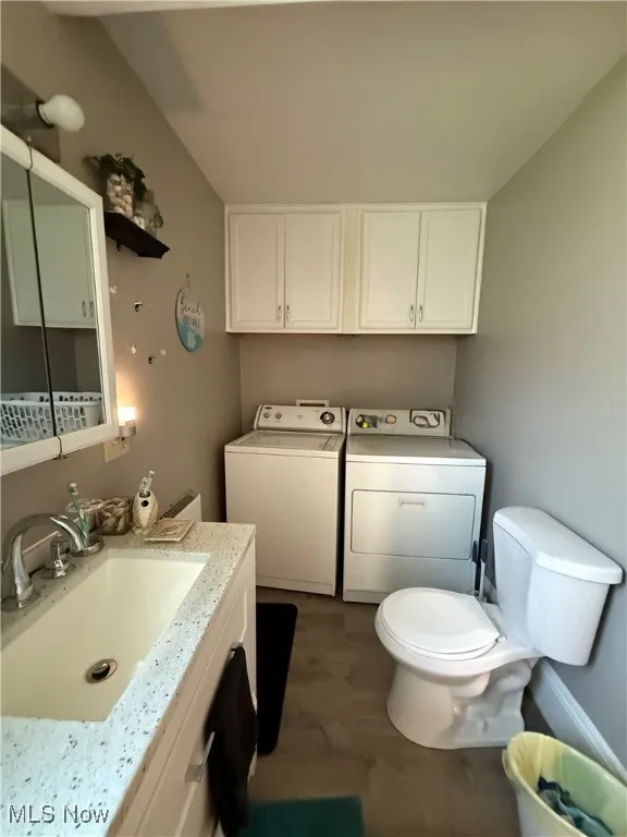 First floor bath featuring washer and clothes dryer, dark wood-type vinly flooring, and vanity