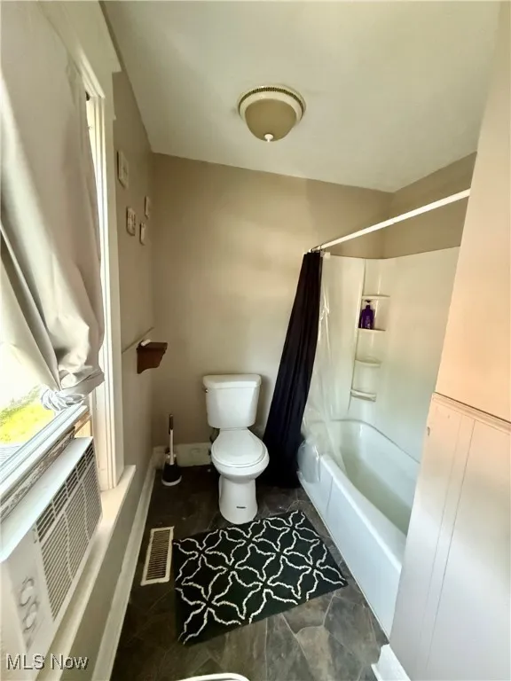 Full bath with shower / bath combo with shower curtain and dark tile patterned vinyl flooring