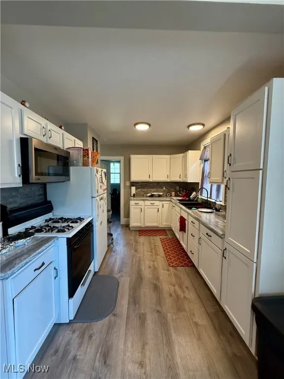 Kitchen with decorative backsplash, white cabinetry, white gas range oven, stainless steel microwave, and light wood-style vinyl floors