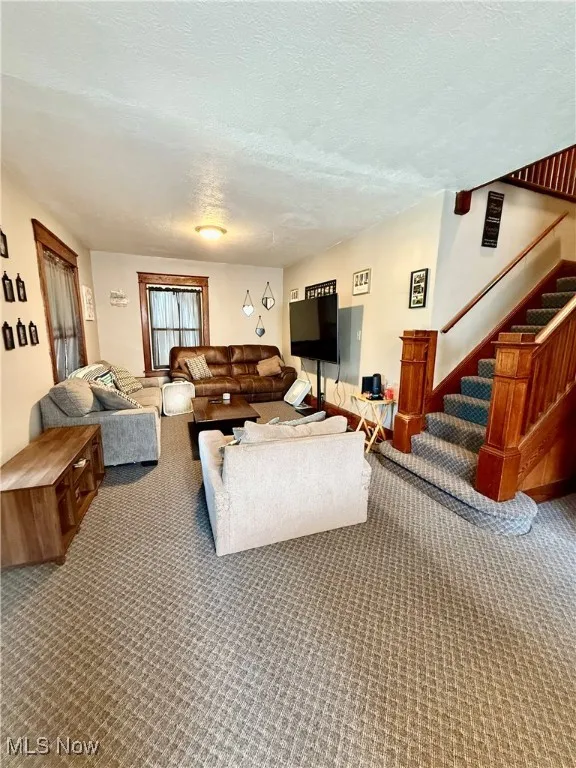 Living area with a textured ceiling, carpet, and stairway
