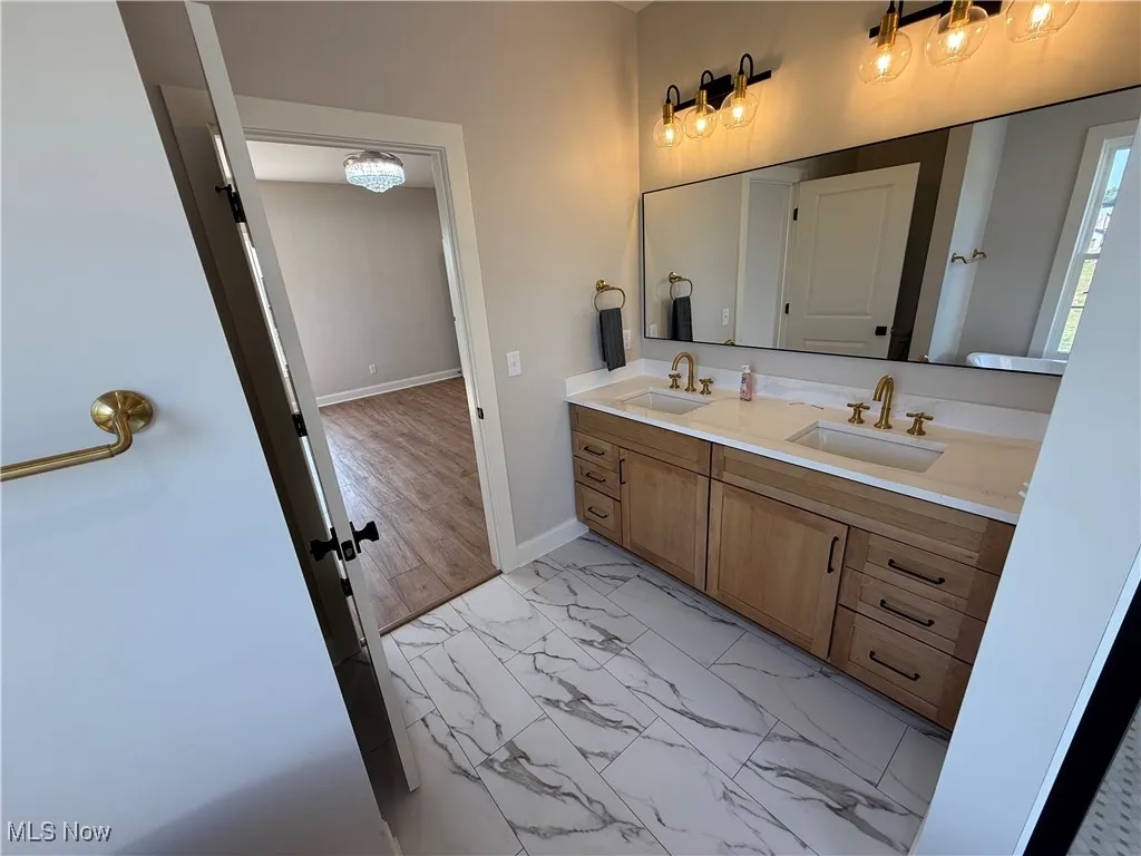 Full bath featuring double vanity and light marble finish flooring