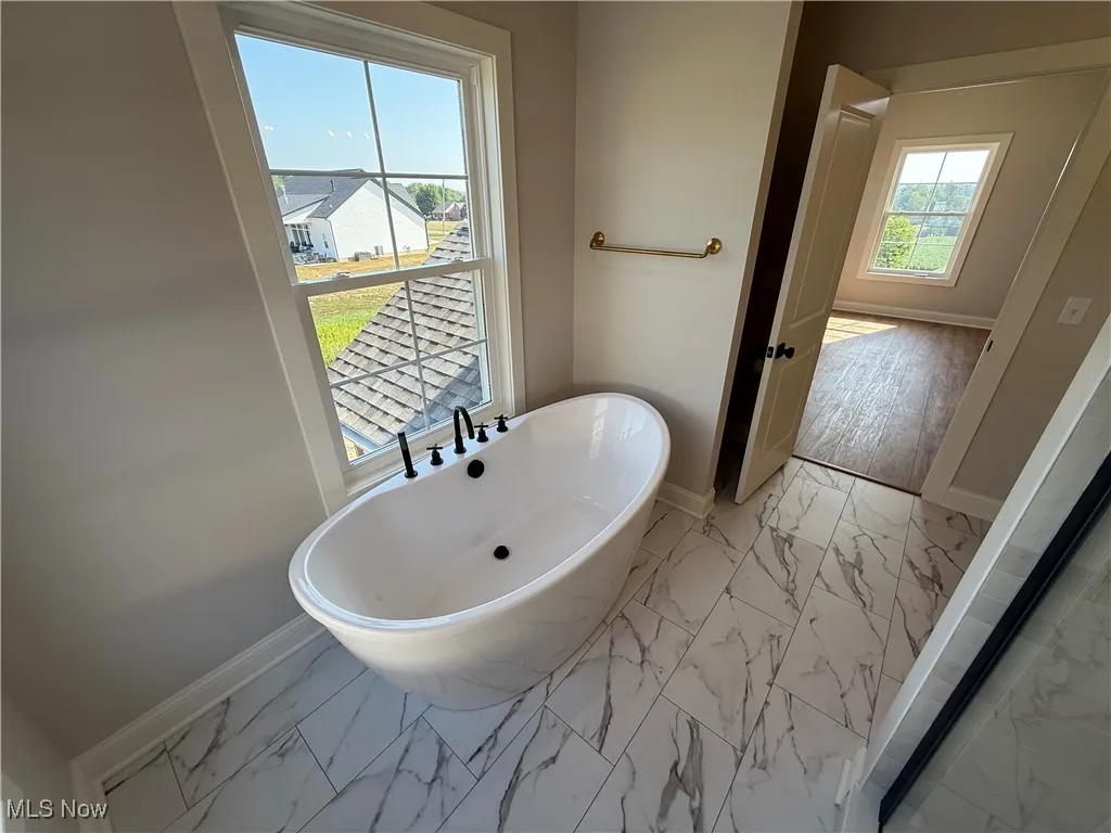 Bathroom featuring light marble finish floors and a soaking tub