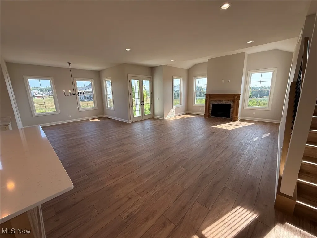 Unfurnished living room featuring a fireplace with flush hearth, dark wood-style floors, recessed lighting, a chandelier, and french doors
