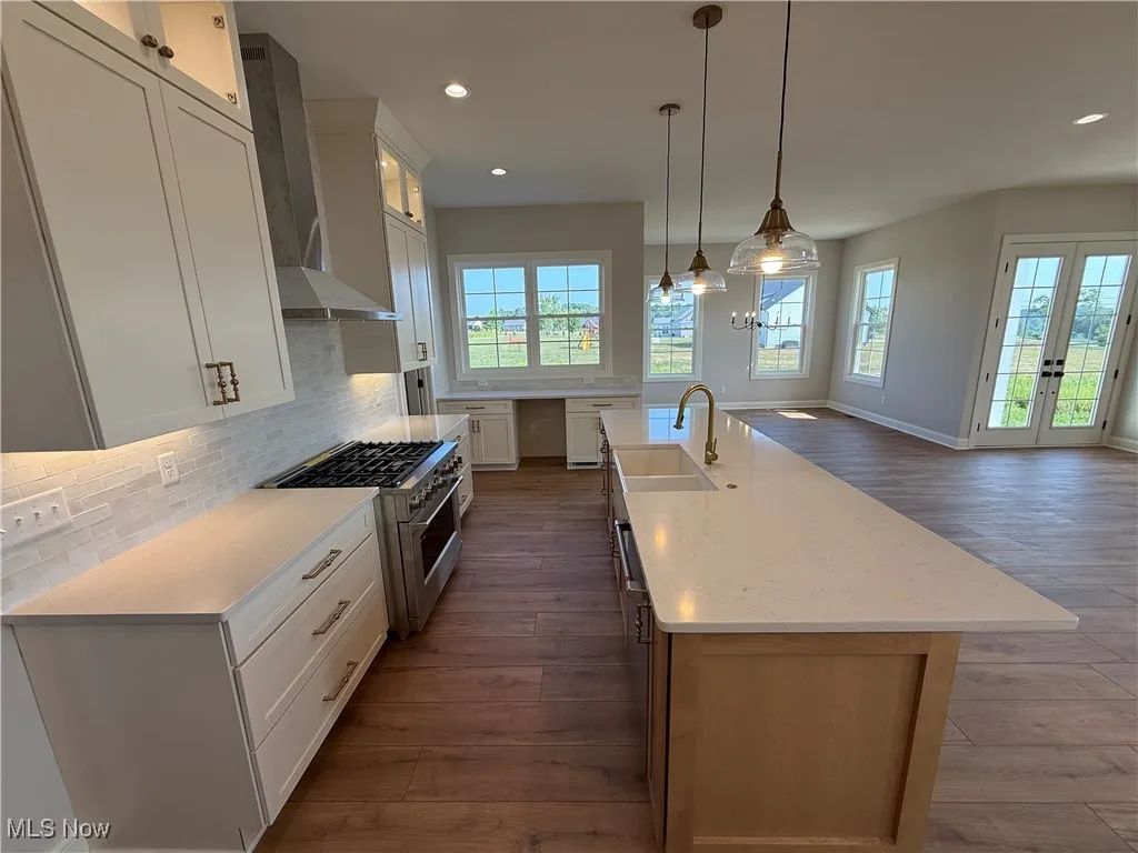 Kitchen featuring high end stainless steel range oven, tasteful backsplash, wall chimney range hood, white cabinets, and dark wood finished floors