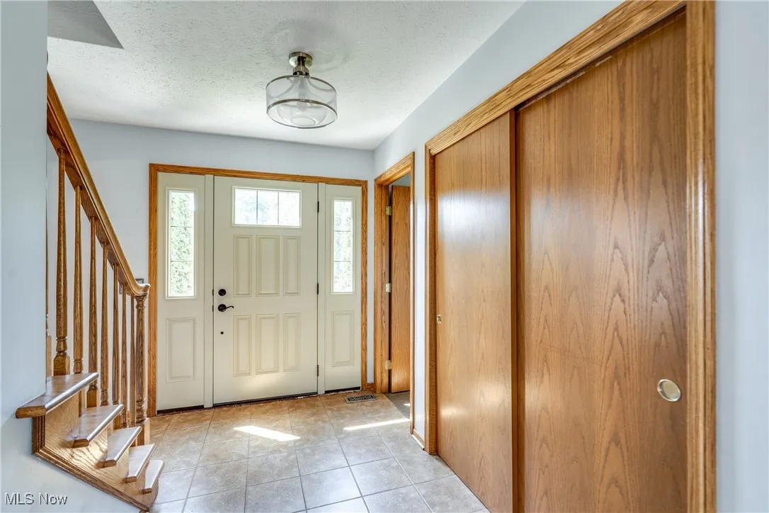 Entrance foyer with a textured ceiling, light tile patterned flooring, and stairs