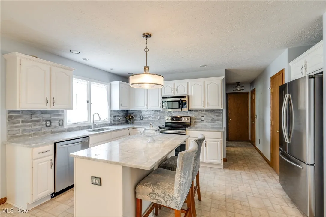 Kitchen with decorative backsplash, stainless steel appliances, hanging light fixtures, light stone countertops, and a breakfast bar area